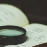 Book with magnifying glass and pen sitting on top, with a globe in the background
